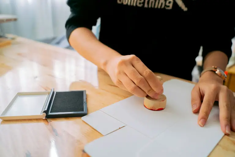 A close-up of a person stamping a document with a red ink stamp, symbolizing official approval or certification.